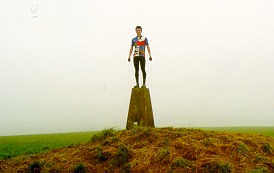 [PHOTO: RJG in cycling kit, standing on trig-point: 13kB]